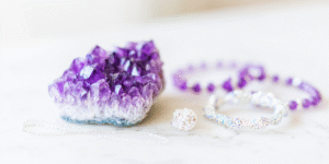 still life of glowing amethyst on white marble surrounded by blurred trinkets and glittering bracelets, representing authenticity beyond adornment