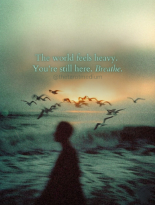 A silhouette stands by a powerful ocean as dawn slowly breaks through heavy clouds, with birds circling overhead, blending endurance and emerging light. The world feels heavy. You're still here. Breathe – this simple quote on the image meets you right in that weight, offering no fix, just acknowledgment and a reminder to stay present.